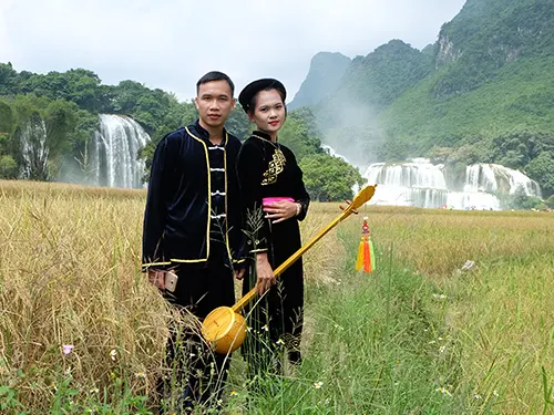 Nghệ sĩ mặc trang phục Tày cầm đàn tính biểu diễn bên ruộng lúa chín dưới chân thác Bản Giốc