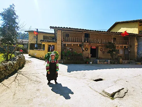 Bà cụ gánh rau qua sân nhà cổ ở bản Lô Chải dưới chân cột cờ Lũng Cú trong tour Hà Giang 2 ngày 3 đêm