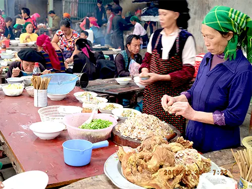 Quầy ẩm thực chợ phiên Đồng Văn với thịt luộc và bàn ăn dài kín khách sáng Chủ nhật